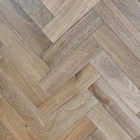 Herringbone parquet flooring planks in a light oak-brown wood finish, showing natural wood grain and texture.
