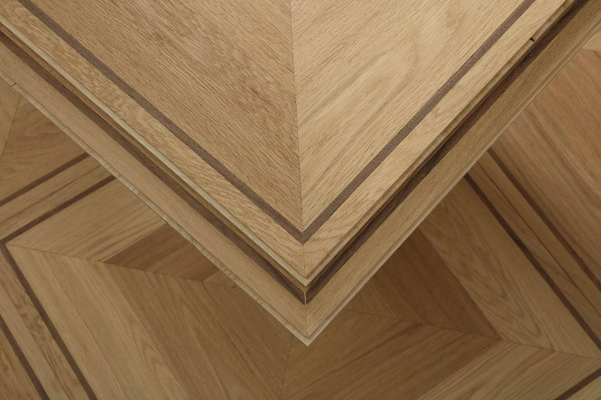 Close-up of a wooden furniture corner showing layered wood veneer panels with a geometric chevron pattern and contrasting dark inlay lines.