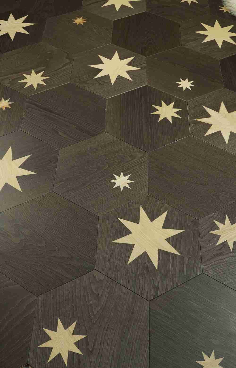 Hexagonal dark wood-look floor tiles with light beige star inlays of varying sizes.