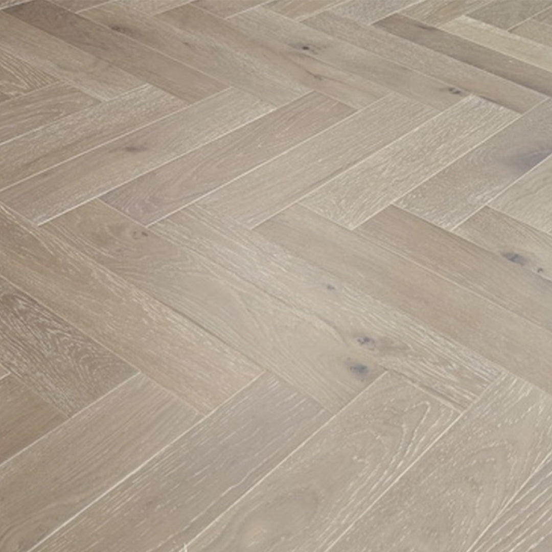 Light oak herringbone wood flooring planks arranged in a classic parquet pattern, showing natural wood grain and subtle knots.