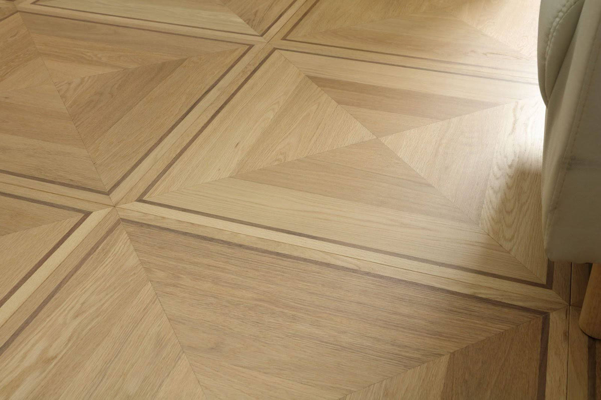 Light natural wood geometric parquet flooring with a chevron and triangular pattern, showing a warm beige tone and visible wood grain texture.