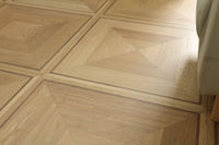 Light natural wood geometric parquet flooring with a chevron and triangular pattern, showing a warm beige tone and visible wood grain texture.
