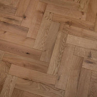Herringbone parquet flooring made of natural oak wood planks with visible grain and knots, arranged in a classic interlocking pattern.