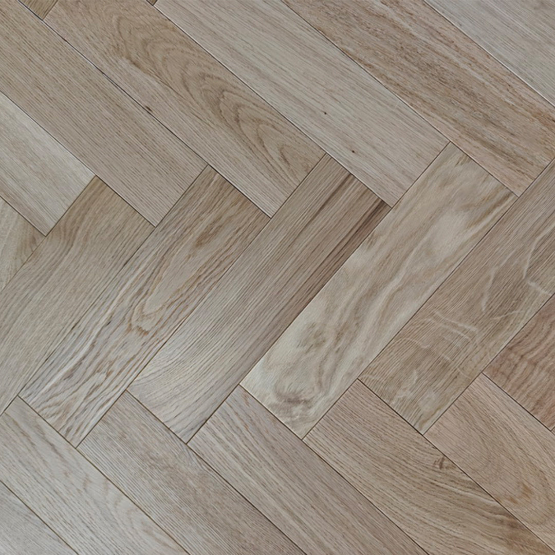 Light oak wood flooring planks arranged in a herringbone pattern, showing natural wood grain and warm beige tones.